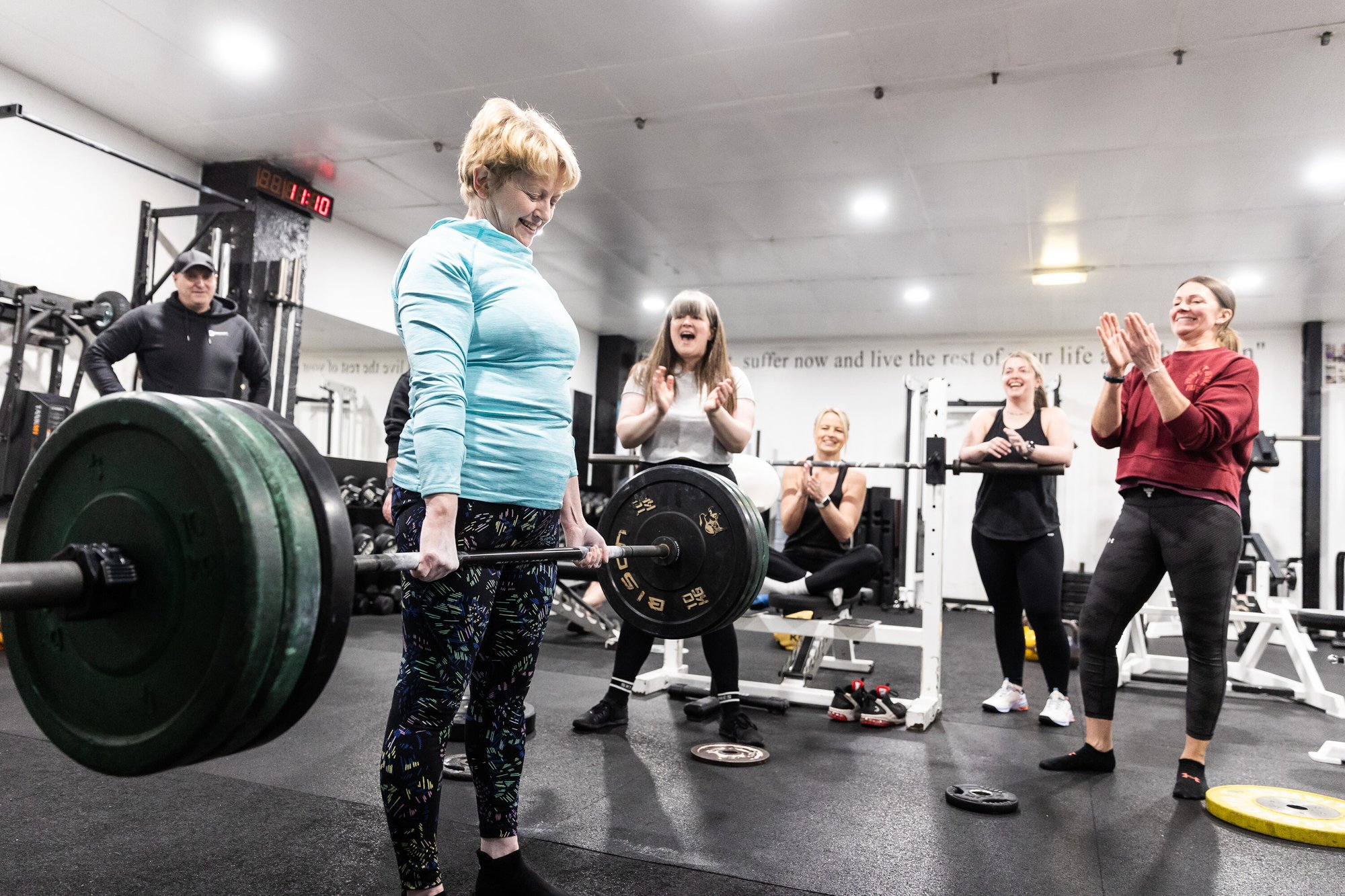 A group of people in a gym cheering on a woman deadlifting