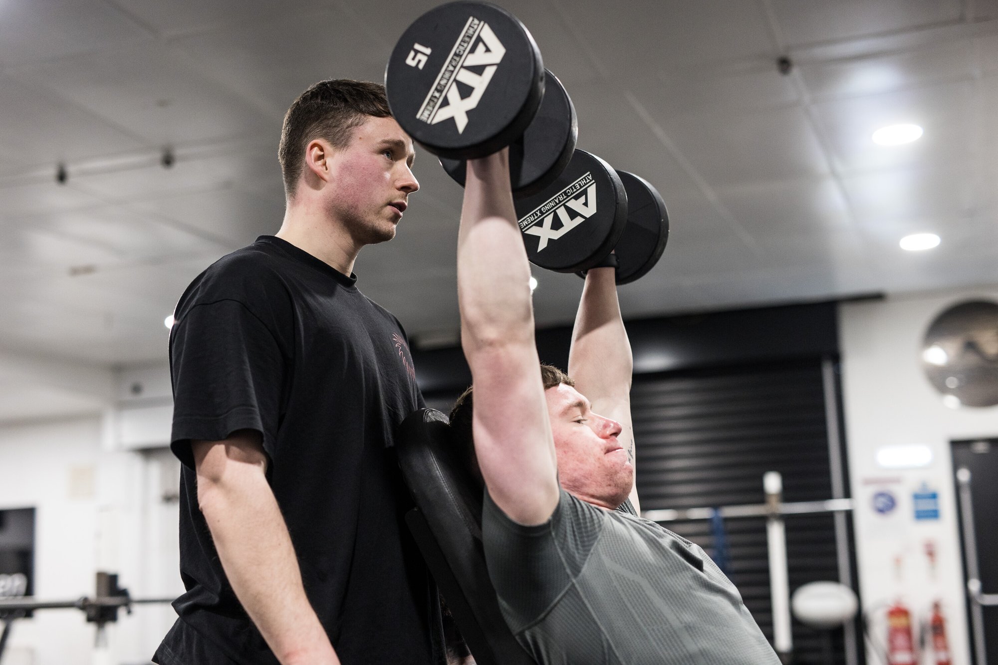 Man lifting dumbbells in a gym with a personal trainer